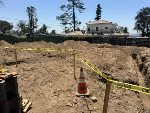 Continued concrete wall forming with rebar and black drainage pipe continuation visible through construction area, showing drainage system installation for Altadena hillside residence.
