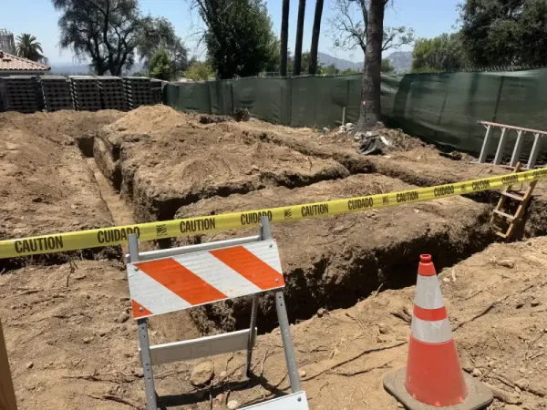 Concrete forming in progress for retaining wall with visible rebar reinforcement and black drainage pipe being installed through hillside slope on Altadena fire rebuild site.