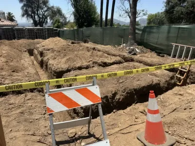Concrete forming in progress for retaining wall with visible rebar reinforcement and black drainage pipe being installed through hillside slope on Altadena fire rebuild site