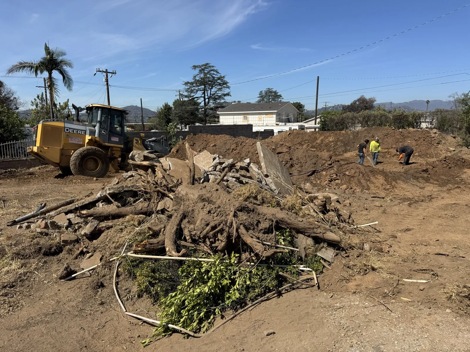 Tree stump and root removal at the Glenrose Avenue Altadena fire rebuild site with a Deere 644K wheel loader and dirt piles during site clearing