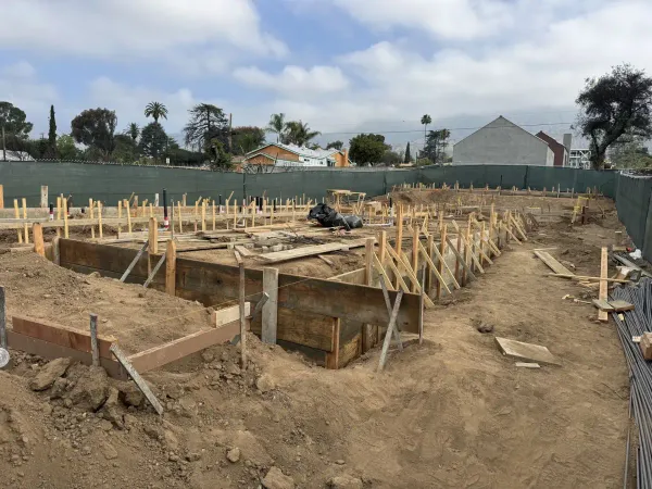 Construction site showing foundation formwork, site grading, and plumbing drainage pipes with rebar materials and wooden boards for concrete forms