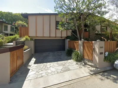 Modern mid-century residence above the Sunset Strip with vertical wood batten siding, flagstone driveway, cedar gates, and mature landscaping