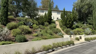 Completed two-story stucco house with a terracotta tile roof behind a concrete retaining wall and stepped entry path on the steep landscaped Redcliff Street hillside in Silver Lake