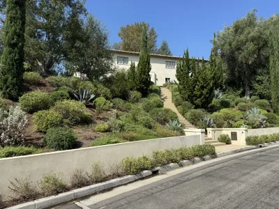 Completed two-story stucco house with a terracotta tile roof behind a concrete retaining wall and stepped entry path on the steep landscaped Redcliff Street hillside in Silver Lake